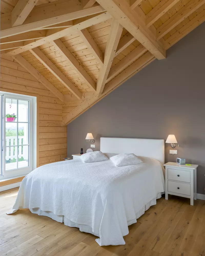 Schlafzimmer mit sichtbarer Dachkonstruktion aus Holz, Doppelbett mit weißer Bettwäsche und Zugang zum Balkon
