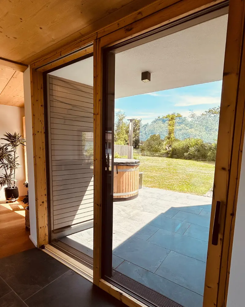 Innenansicht einer großen Schiebetür aus Holz mit Blick auf Terrasse und Garten, Teil des nachhaltigen Fensterkonzepts