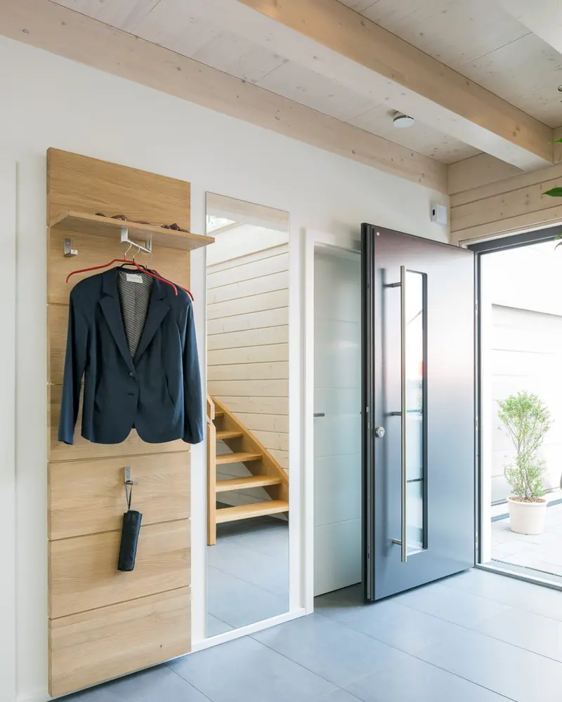 Moderner Eingangsbereich mit Garderobe, Holzoberflächen und hochwertiger Haustür in einem individuell geplanten Holzhaus.