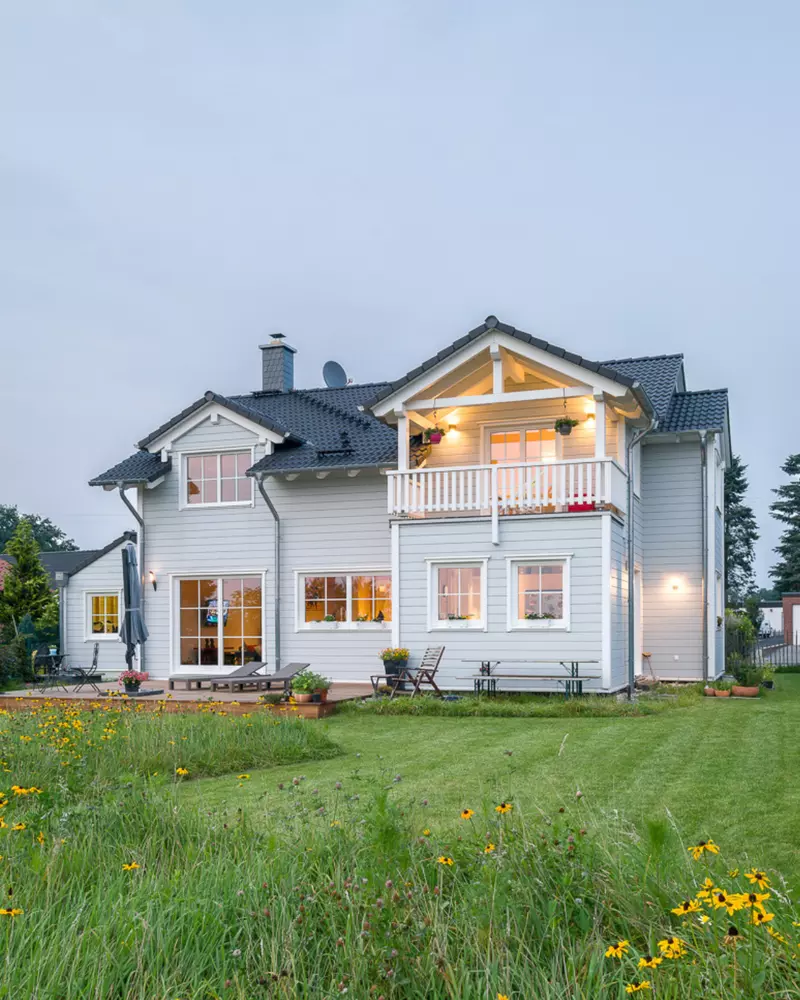 Rückansicht eines Holzhauses mit Balkon, Terrasse und Gartenfläche im Abendlicht