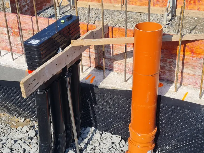 Baustelle mit vorbereiteten Leitungsrohren, orangefarbenem Kanalrohr, Schalung und Bewehrung vor dem Betonieren der Bodenplatte.