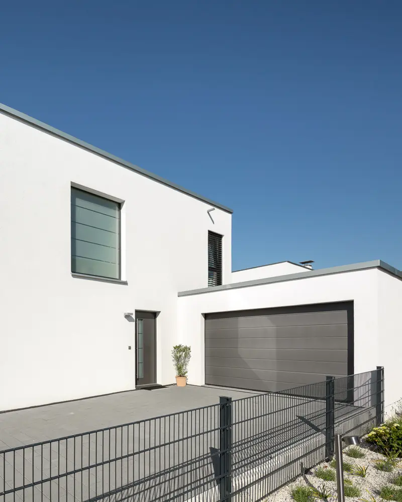 Garage mit gepflasterter Hoffläche und Hauseingang eines modernen Wohnhauses als Beispiel für häufig unterschätzte Baunebenkosten.