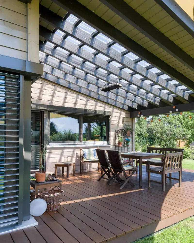 Überdachte Holzterrasse mit Sitzbereich, transparenter Dachkonstruktion, Holzfassade und Blick in den grünen Garten.