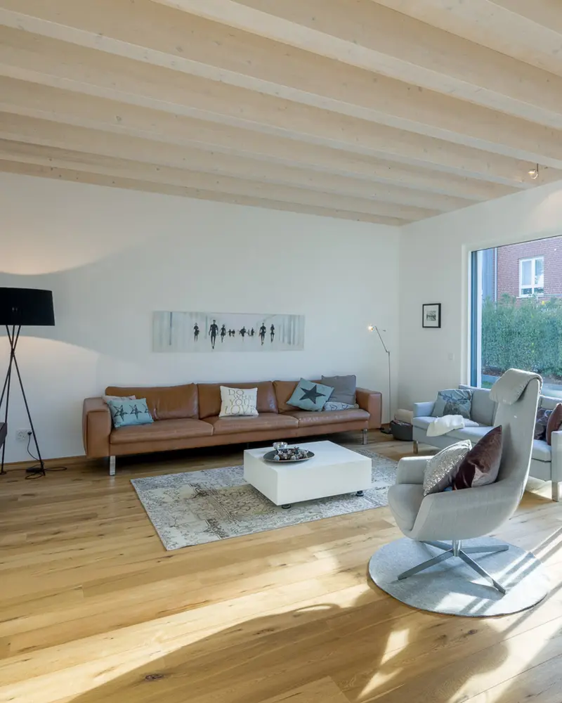 Lichtdurchflutetes Wohnzimmer mit heller Holzdecke, Parkettboden und moderner Einrichtung. Das Holz ist dezent integriert und wirkt klar und zeitlos statt rustikal.
