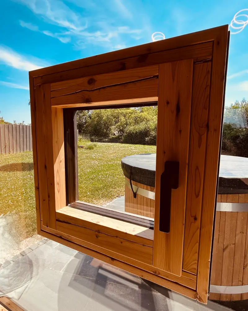 Detailaufnahme eines kleinen Holzfensters aus recycelten Balken mit sichtbarer Maserung und handwerklichen Strukturen