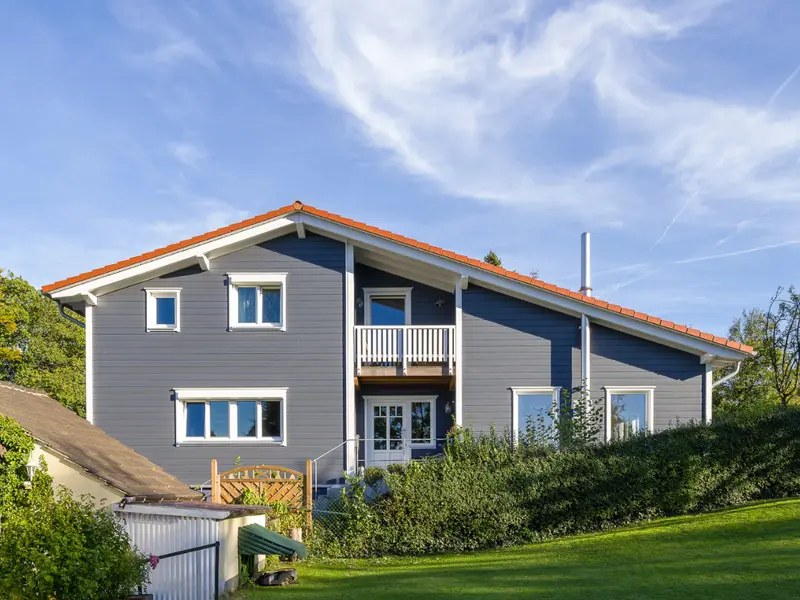 Individuell geplantes Holzhaus von Stommel Haus auf leicht geneigtem Grundstück mit großer Rasenfläche, gepflegter Bepflanzung und markanter Holzfassade unter blauem Himmel.