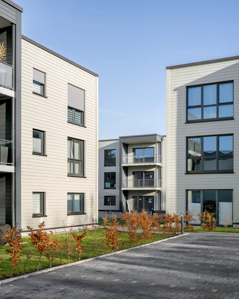 Mehrere moderne Wohngebäude in Holzbauweise mit Innenhof und begrünten Außenanlagen. Symbolbild für die Projektphasen eines Bauvorhabens von Planung, Genehmigung und Produktion bis zur Fertigstellung.