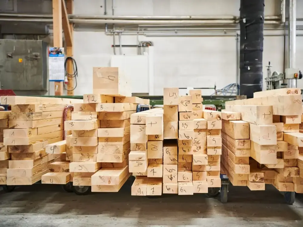 Gestapelte, nummerierte Holzbalken als nachhaltige Baumaterialien in der Produktion von Stommel Haus.