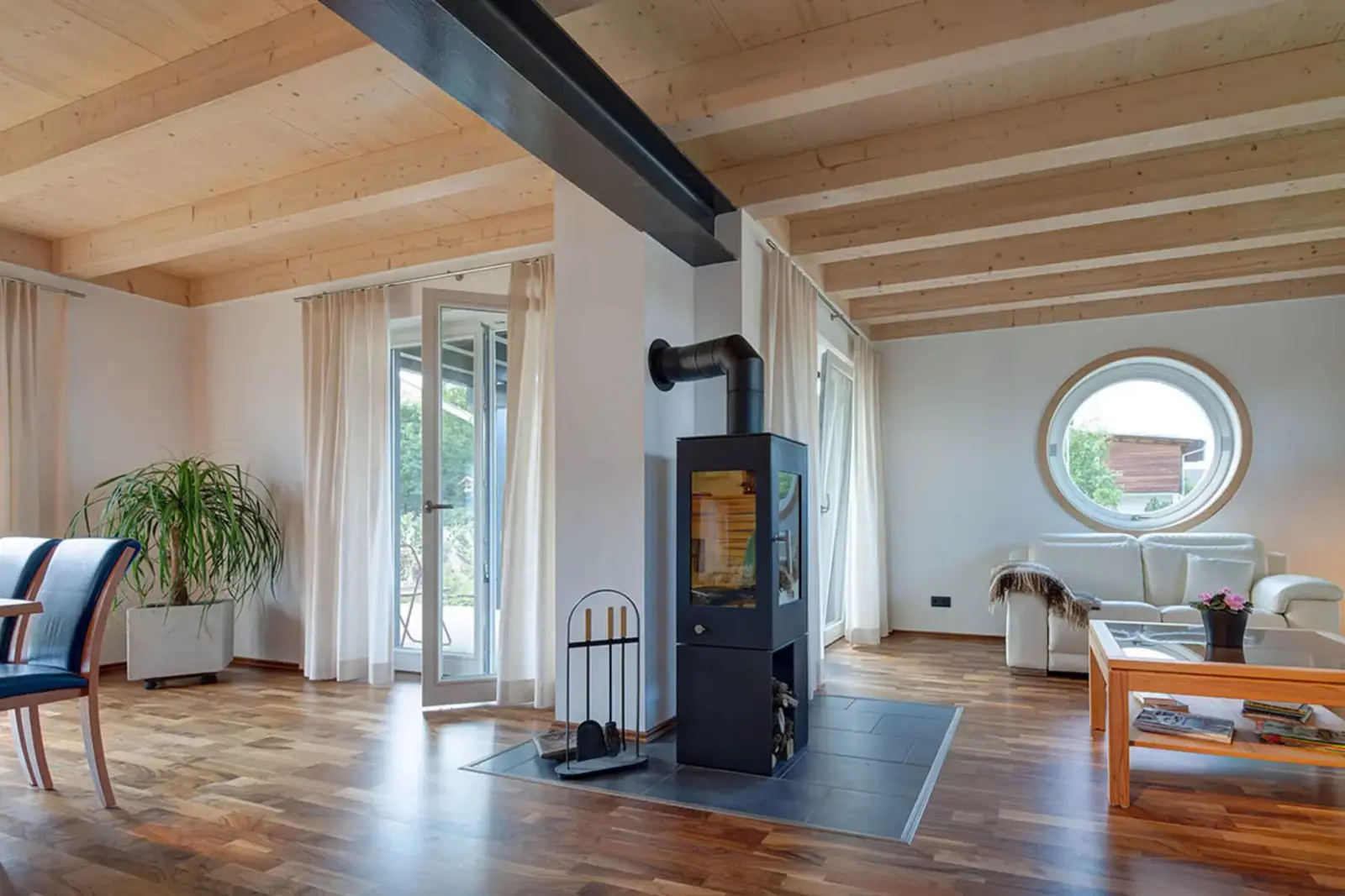 Ein Bereich eines Raumes von einem der schlüsselfertigen Holzhäuser von Stommel Haus. Der Innenraum zeigt einen Kamin, Stühle und ein rundes Fenster.