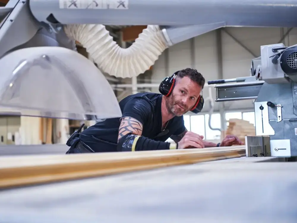 Ein Mitarbeiter von Stommel Haus bearbeitet ein Holzbauteil an einer Kappsäge in der Produktionshalle.