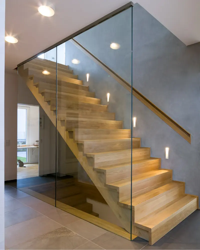 Offene Holztreppe mit Glasgeländer in einem modernen Holzhaus. Sichtbare Holzstufen treffen auf zurückhaltende Wandgestaltung und zeitgemäße Innenarchitektur.
