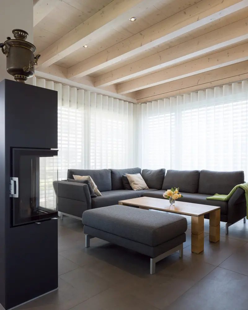 Gemütlicher Wohnbereich mit Kaminofen, großen Fensterflächen und sichtbaren Holzdecken in einem modernen Holzhaus.