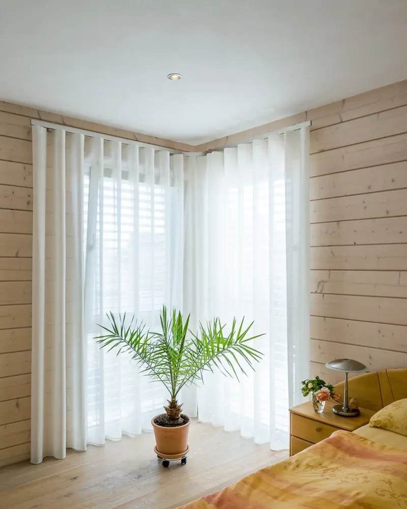Helles Schlafzimmer mit Holzwand, großem Fensterbereich und natürlicher Innenraumgestaltung im Holzhaus.