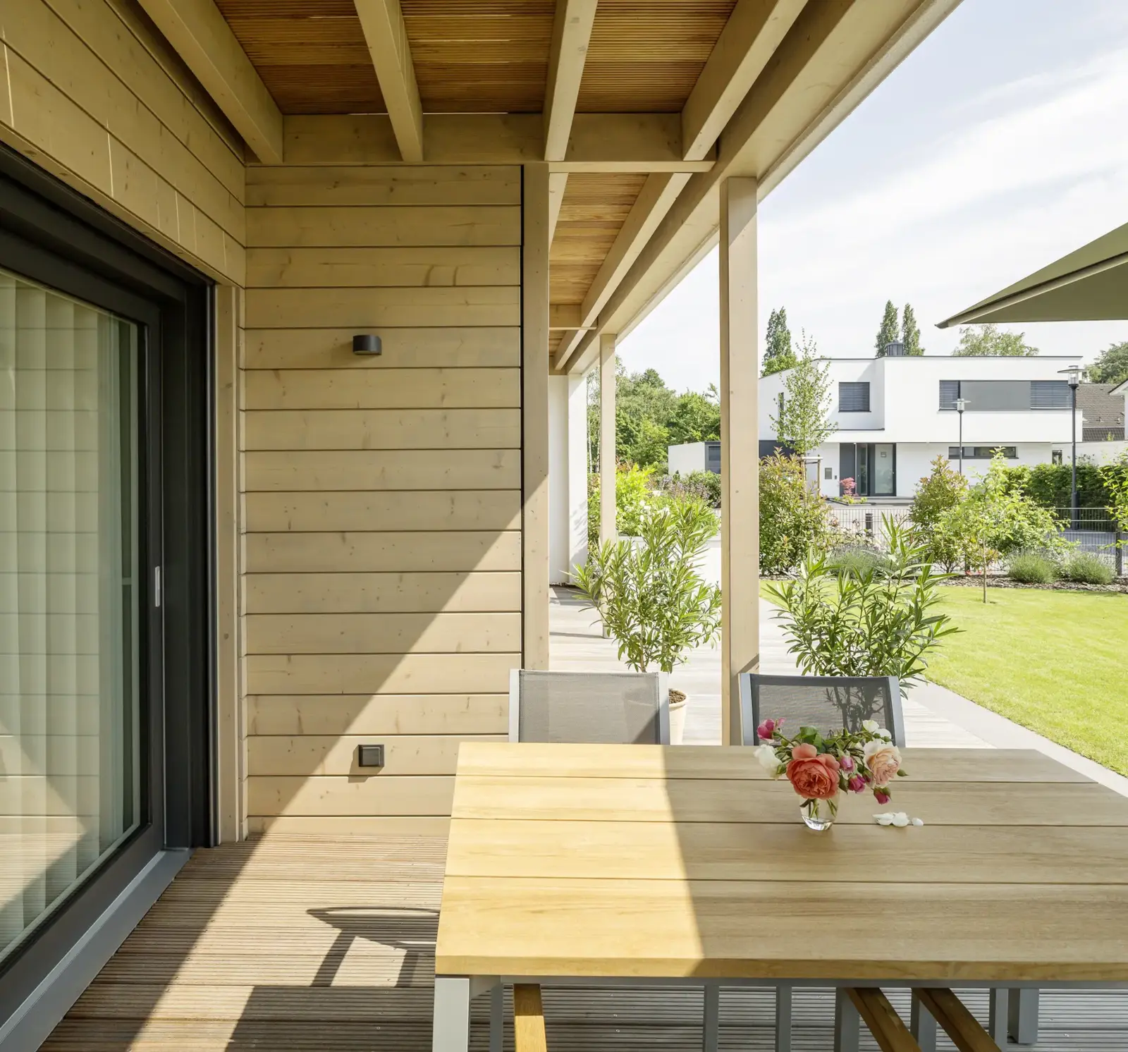 Stommel Haus: überdachte Holzterrasse mit gedecktem Tisch, Rosenstrauß und Blick in den Garten.