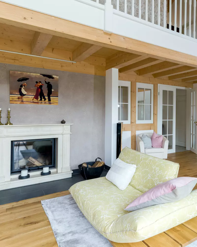 Wohnzimmer mit Kamin, Sitzmöbel, sichtbaren Holzbalken und Galerieebene im oberen Bereich