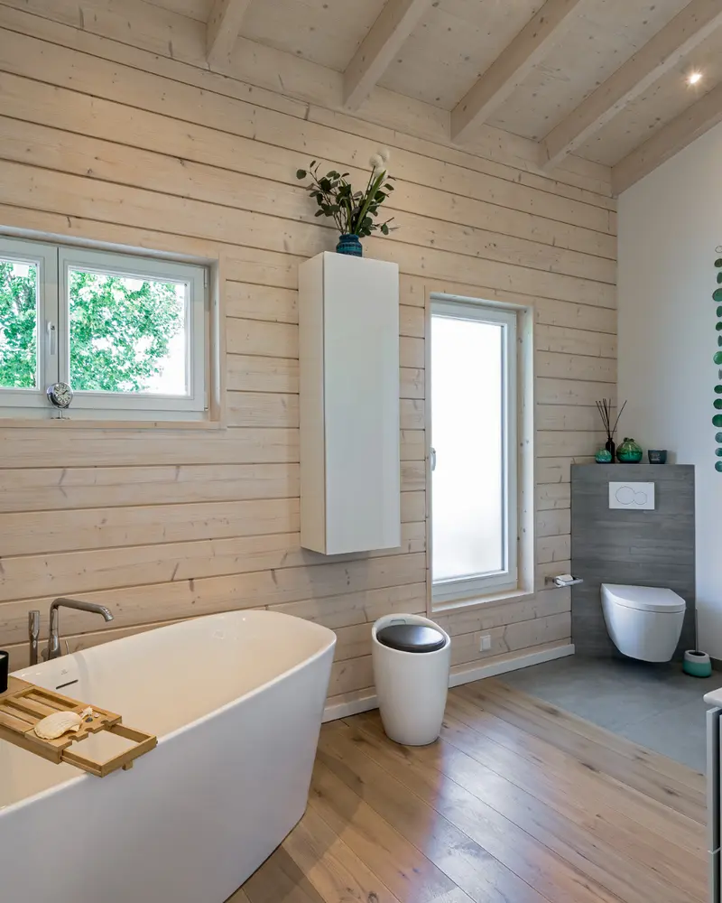 Badezimmer mit freistehender Badewanne, Waschtisch, WC, Holzinnenwand und sichtbarer Verbindung von Gestaltung und technischer Planung.