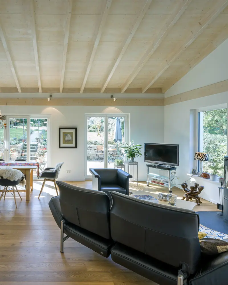 Wohnbereich mit Holzdecke, großen Fenstern, Sofa und Essplatz in einem fertigen Stommel Haus als Ergebnis einer abgestimmten Bauplanung.
