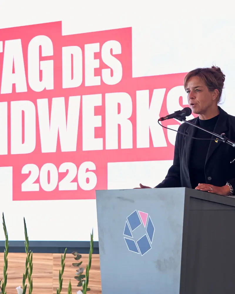 Eine Person steht an einem grauen Rednerpult mit Mikrofon. Im Hintergrund zeigt eine große Leinwand den Schriftzug „Tag des Handwerks 2026“ in roten und weißen Buchstaben.