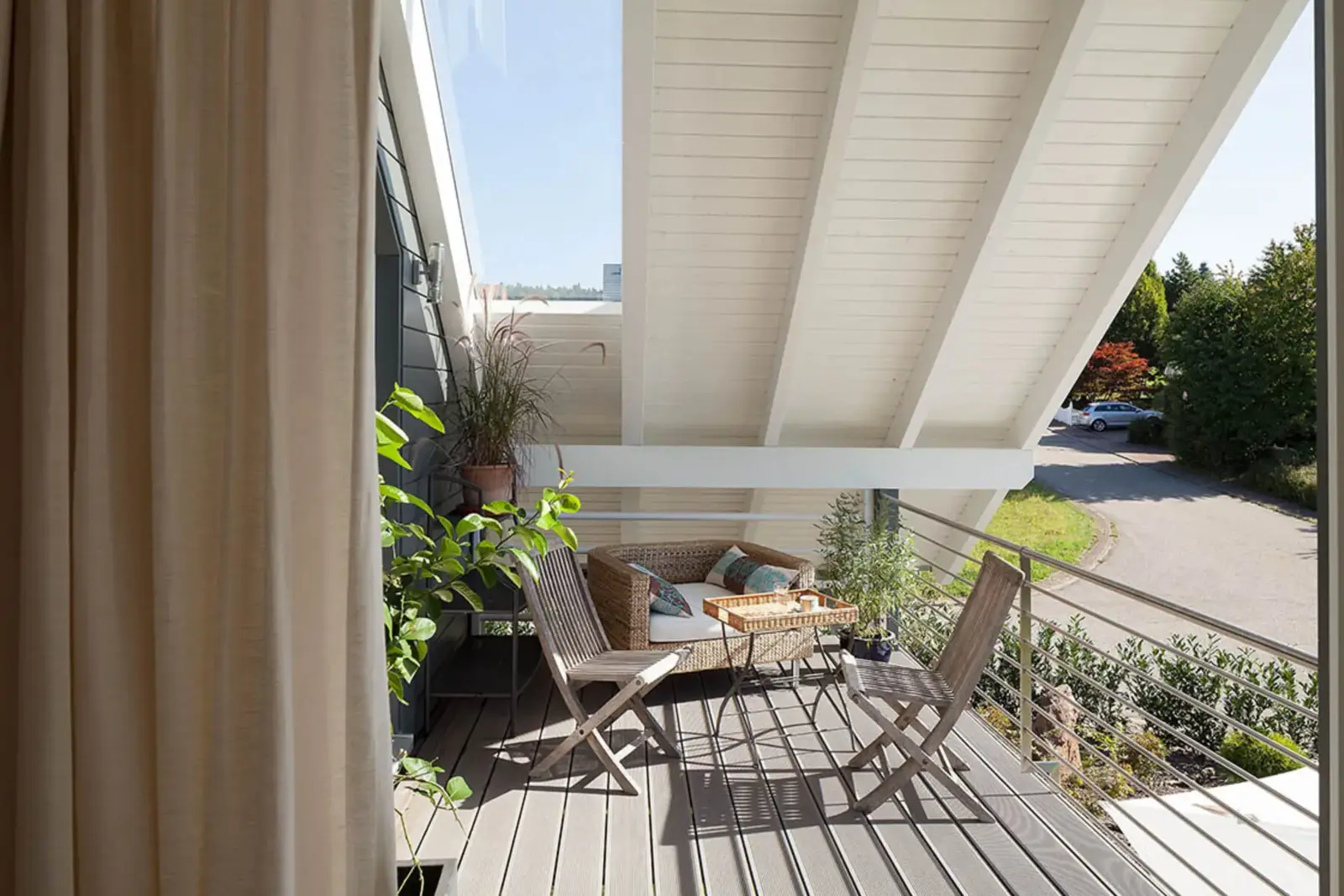 Ein Balkon eines der schlüsselfertigen Holzhäuser von Stommel Haus. Zu sehen ist das Schrägdach über dem Balkon, ein Esstisch mit Stühlen und ein Vorhang.