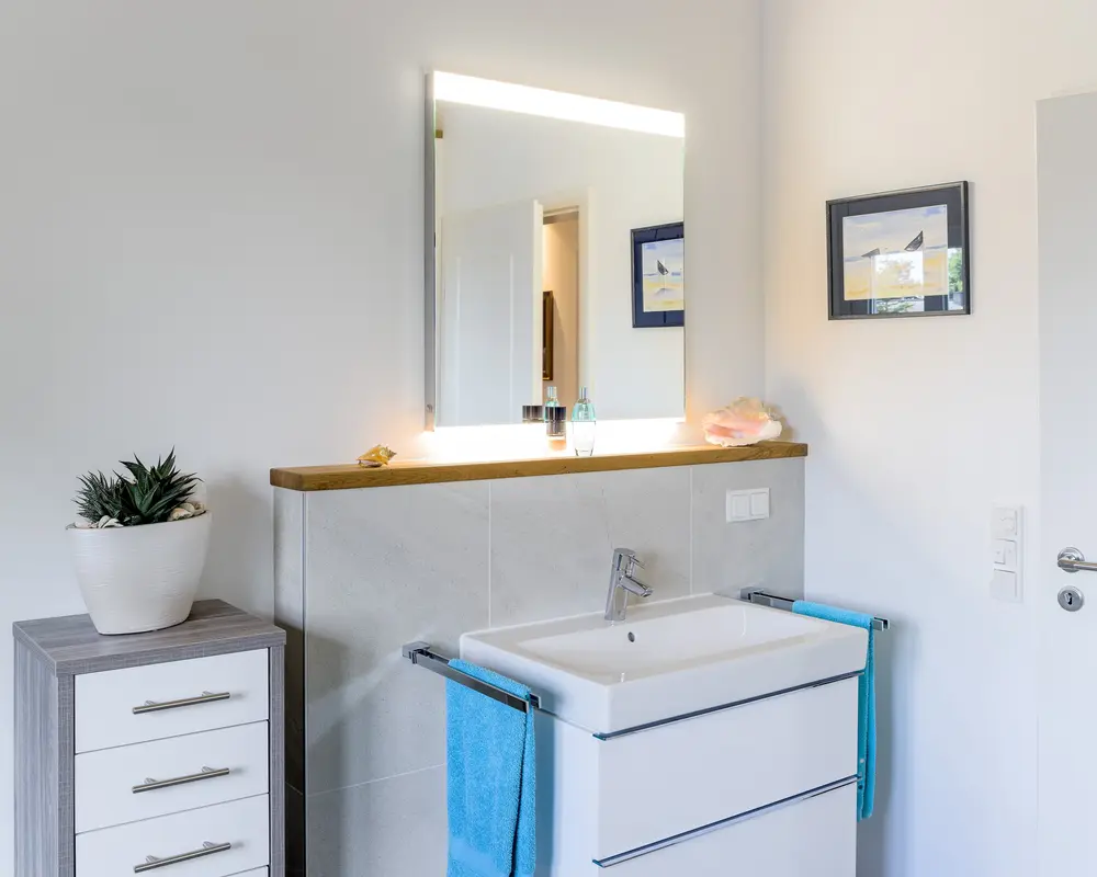 Ein Badezimmer eines kleinen Holzhauses für Senioren, ein Spiegel hängt an der Wand und mehrere Schränke stehen davor.