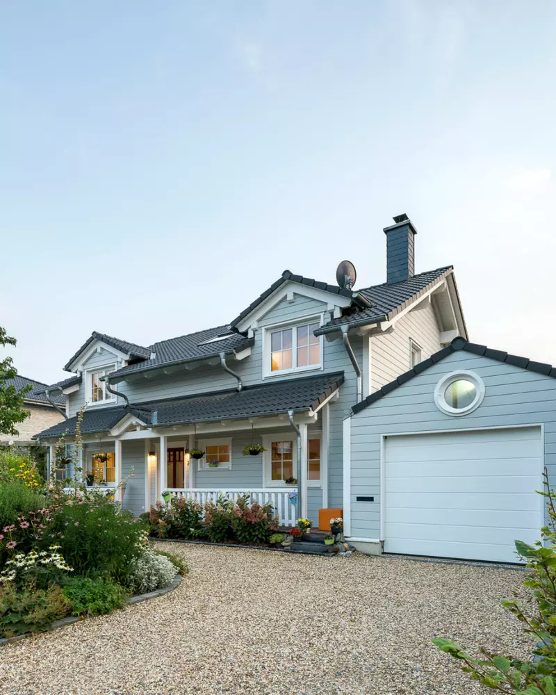 Außenansicht eines Einfamilienhauses mit heller Holzfassade, Veranda, Garage und bepflanztem Vorgarten