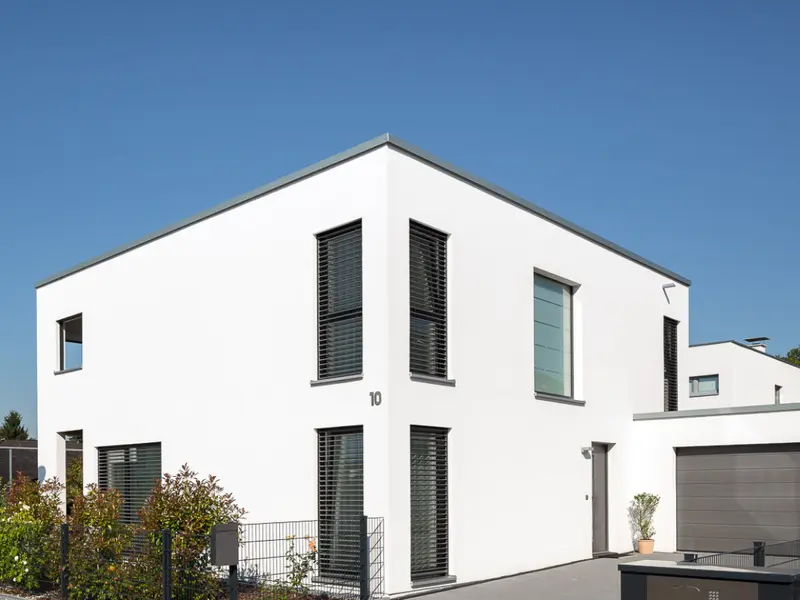 Modernes Einfamilienhaus in klarer Architektur mit Garage, gepflasterter Zufahrt, Einfriedung und angelegten Außenbereichen vor blauem Himmel.