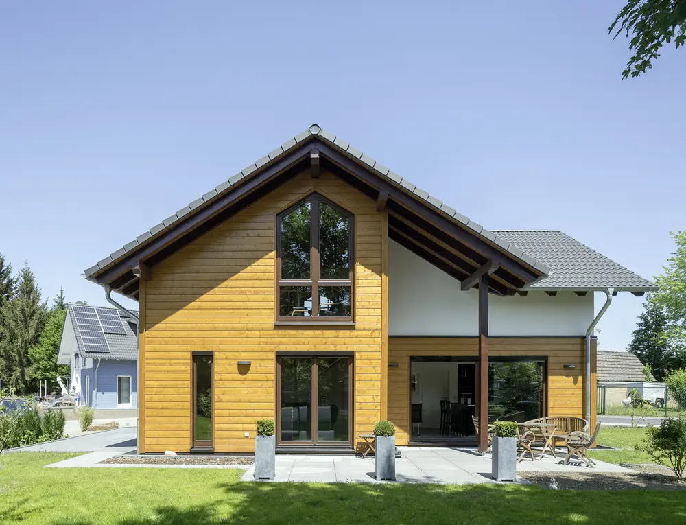 Holzhaus Pflege: gepflegte gelbe Holzfassade eines Stommel-Haus-Holzhauses mit steilem Giebeldach und Terrasse.